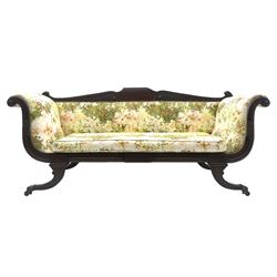 Regency period mahogany settee, scroll and lobe carved cresting rail, upholstered in floral patterned fabric with squab cushion, double scrolled and shaped ends, splayed moulded supports with brass cups and castors