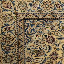 Central Persian fine Nain hand-knotted rug, ivory ground, with a central shaped floral medallion with pendants, surrounded by scrolling foliate and floral motifs incorporating rosettes, palmettes and delicate vine work in blue, cream and beige tones, enclosed by blue spandrels and an ivory border with repeating palmettes and meandering vines, flanked by floral guard stripes, with cotton fringes
