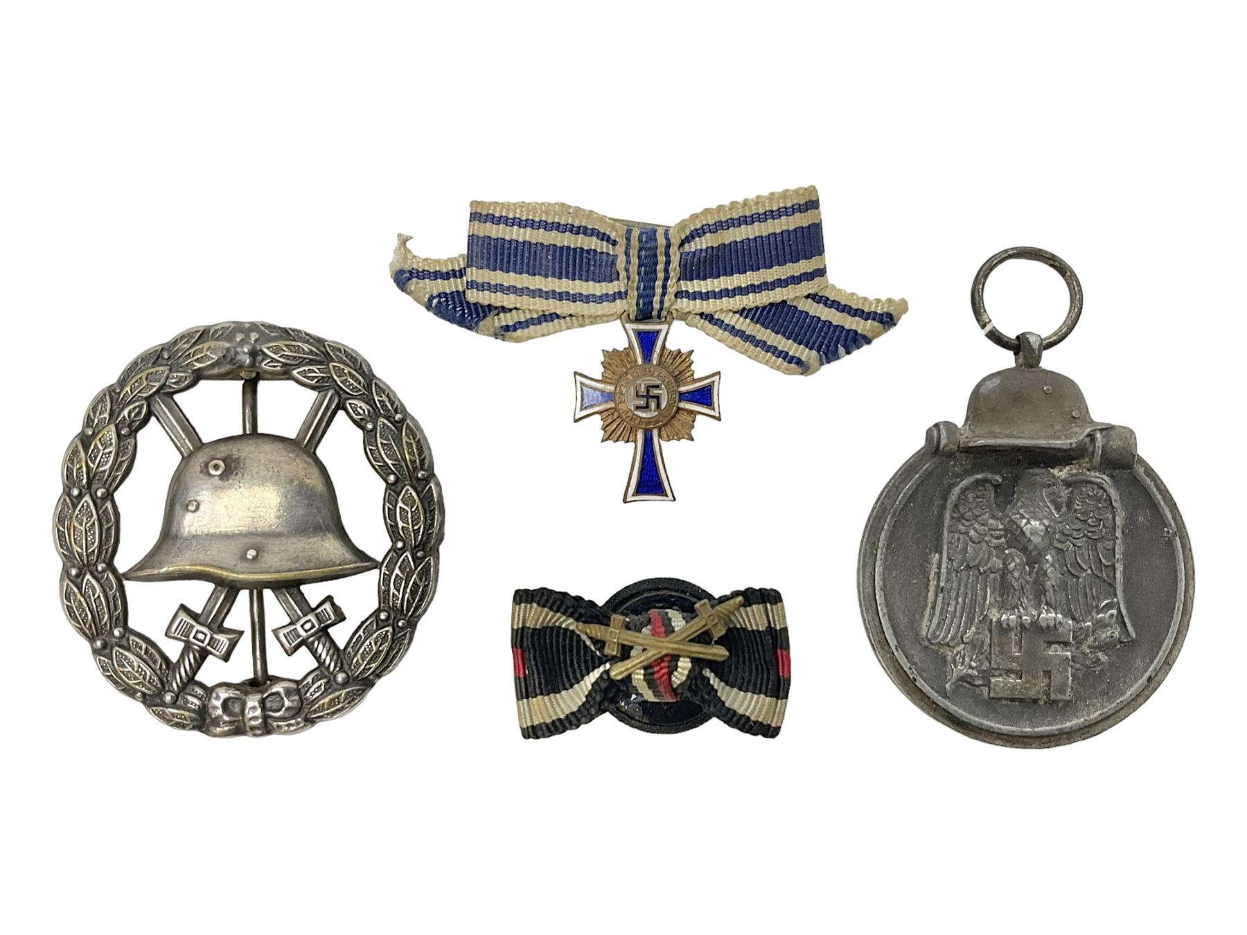 Four German awards - pre-WW2 two-position button hole ribbon for 1914 Iron Cross; WW1 wound badge open back cut-out version with silvered finish; miniature version Mother's Cross with ribbon bow; and The Eastern Medal, officially the Winter Battle in the East 1941–42 Medal (4)