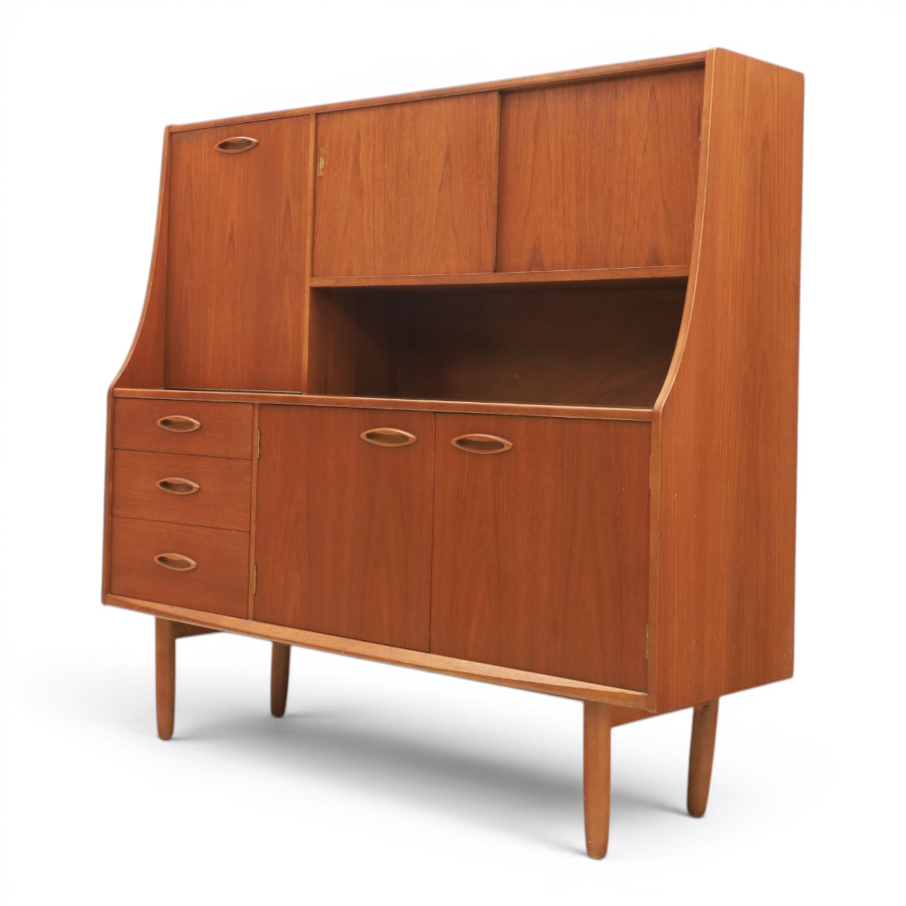 Jentique - mid-20th century teak highboard, fall front cabinet next to a sliding door cupboard above and open recess, the lower section with cabinet doors and three graduated drawers, raised on cylindrical legs