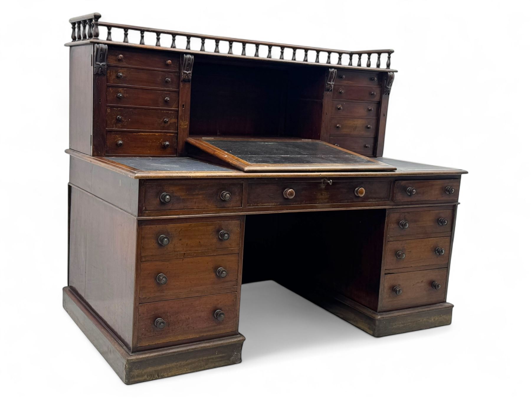 Large Victorian mahogany Registry/Dickens’ desk, spindle gallery top, one side with five small drawers and the other with blind cupboard drawer, revealing pigeon holes with scroll carved locking side bars on either side, above a hinged and leathered writing slope with three drawers and pigeon holes underneath, above a central locking drawer with key, the pedestals each with four drawers and  turned knob handles, separates into four parts for transport