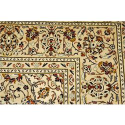Central Persian Kashan hand-knotted carpet, ivory field with central lobed medallion issuing an all-over design of scrolling vines, palmettes, and floral sprays, within conforming spandrels, enclosed by a foliate border, framed by multiped guard stripes, with cotton fringe ends 
