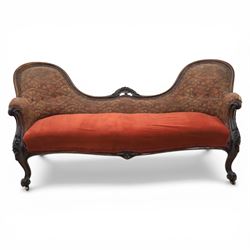 Victorian mahogany framed serpentine sofa, the shaped button upholstered back with central carved foliate cartouche, and scroll arms with carved terminals, over upholstered red seat, upon carved cabriole supports with castors