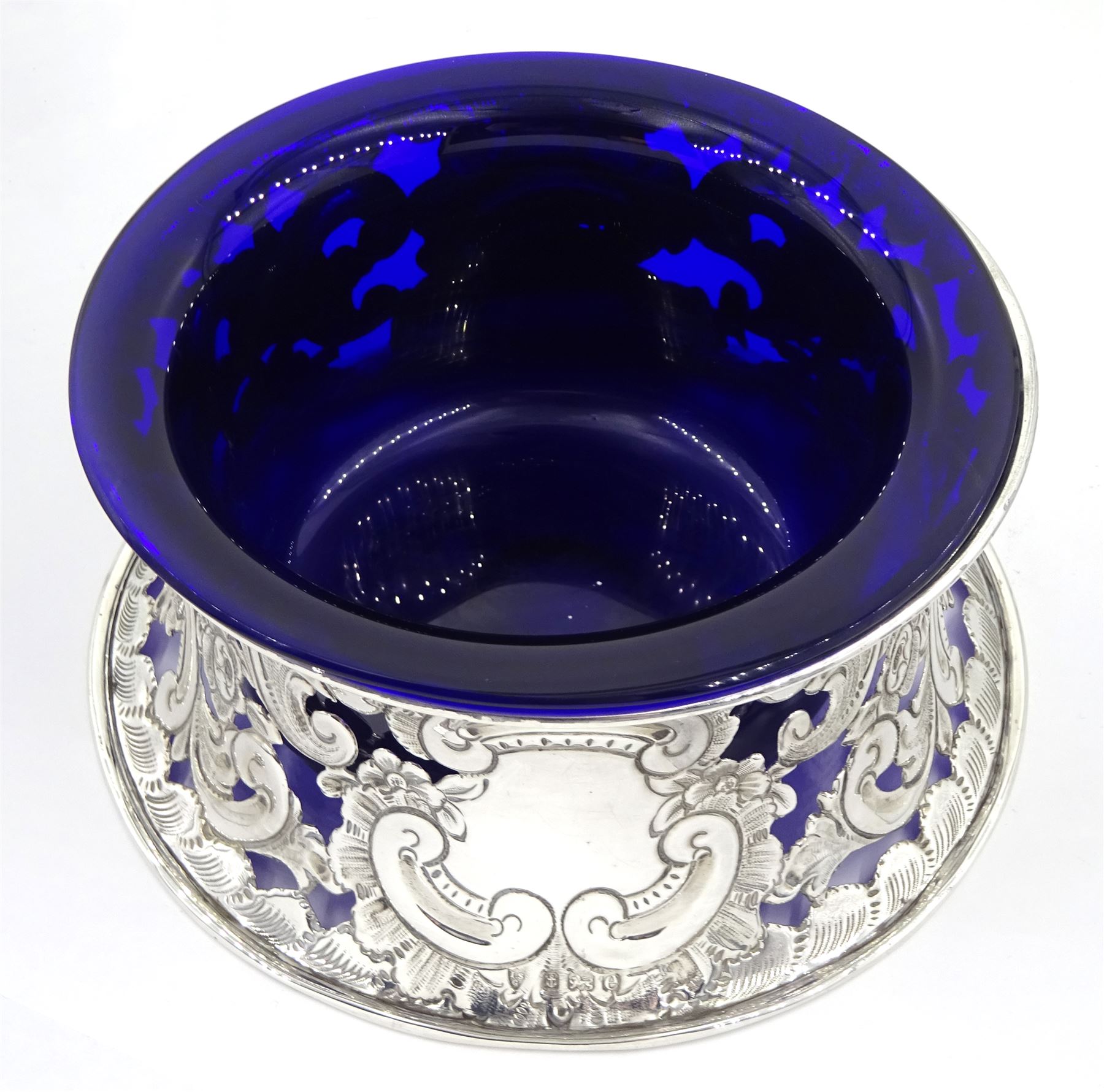 Edwardian silver dish ring in the Irish manner, of circular waisted form, embossed and pierced throughout with flower heads and foliate and C scrolls, hallmarked I S Greenberg & Co, Birmingham 1904, with accompanying blue glass liner, upper rim D17.5cm, approximate weight 6.84 ozt (213 grams)