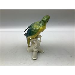 Karl Ens porcelain figure of a parrot, modelled with yellow breast, blue back and wings and green tail, perched upon on a blossoming branch, with blue printed factory mark beneath, H24.5cm