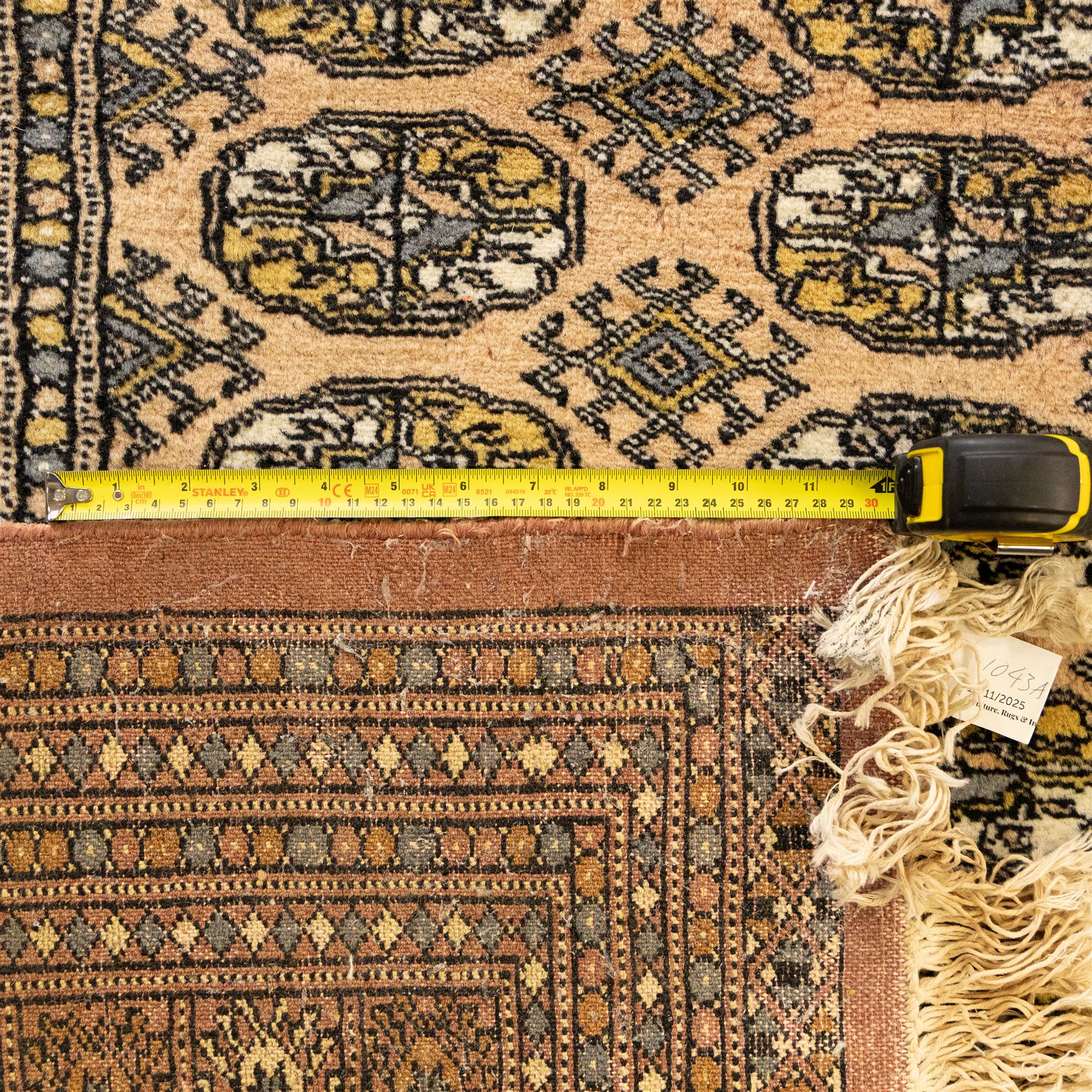 Bokhara rug, rose ground, with multiple rows of ivory and indigo guls enclosed by narrow geometric borders in tones of ivory, grey, and gold