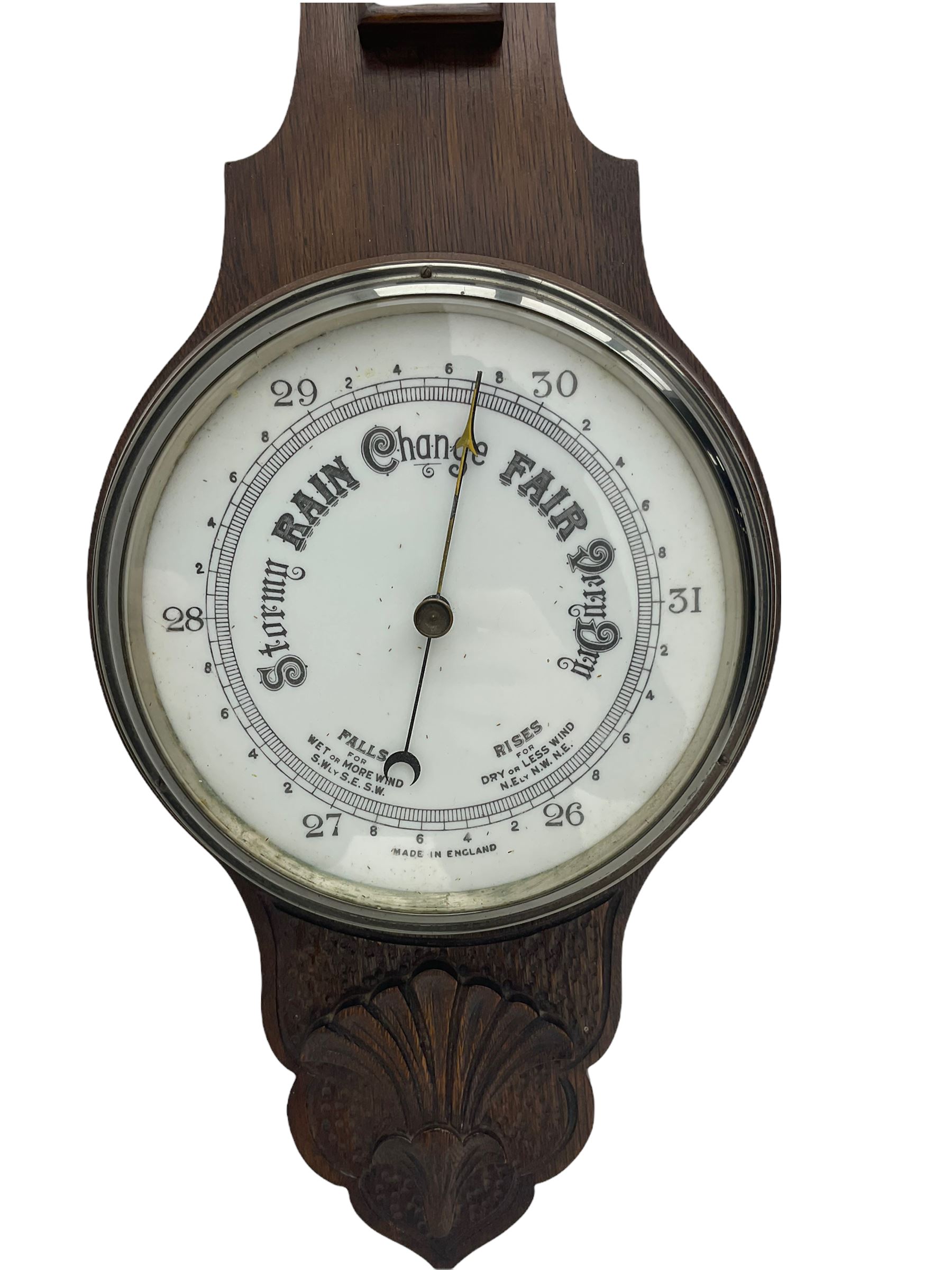 An English carved oak cased aneroid barometer with an 8'' porcelain dial, measuring barometric pressure from 26 to 31.9 inches, weather predictions written in gothic capitals and lower-case script, with a steel indicating hand and brass recording hand within a chrome bezel with a flat bevelled glass, with a spirit thermometer recording the temperature in degrees Fahrenheit and Celsius.



