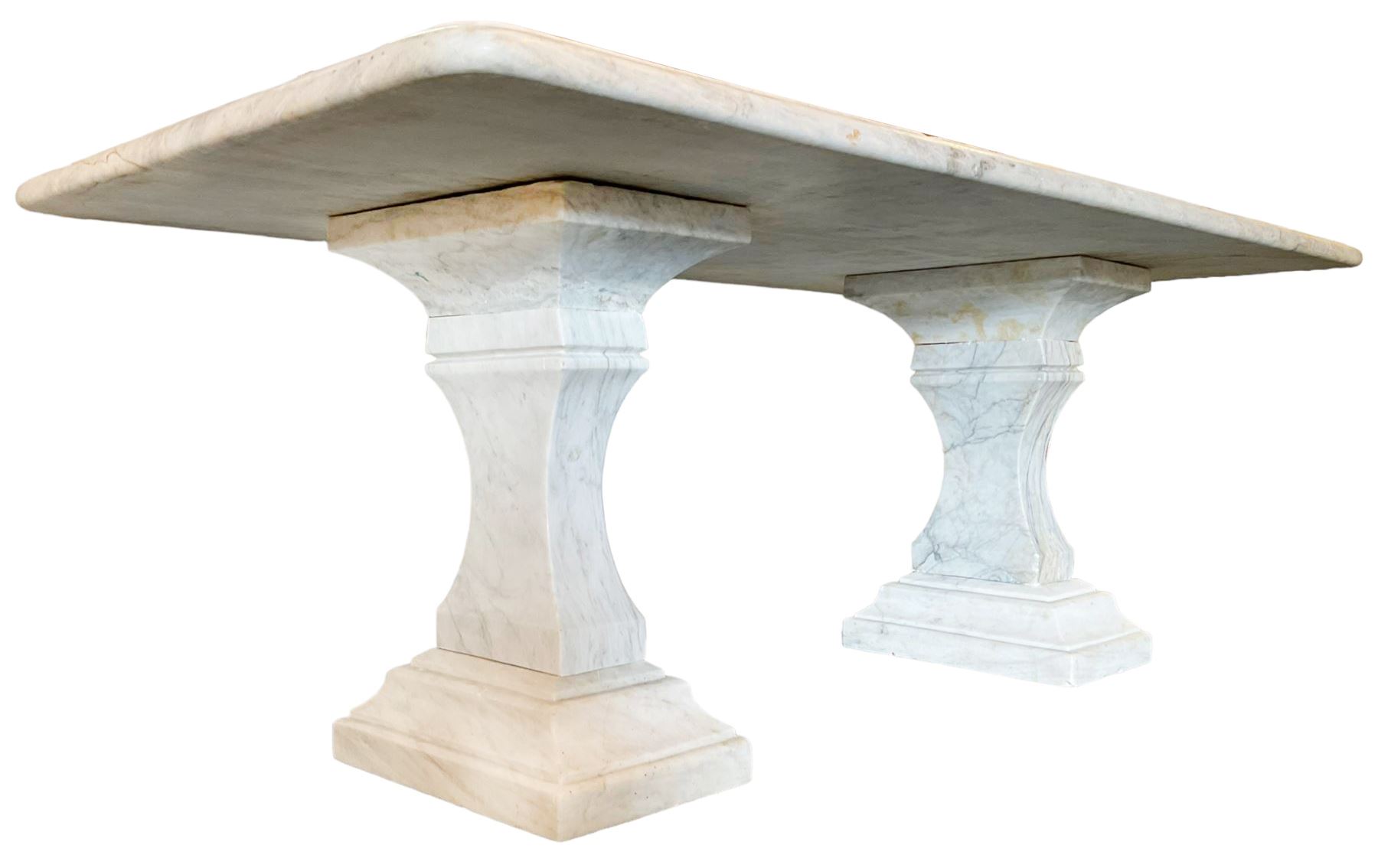 Classical Grecian design Carrera marble centre table, the rectangular single slab top with rounded corners and carved edge, raised on twin pedestals comprised of three pieces with a waisted column on a stepped plinth