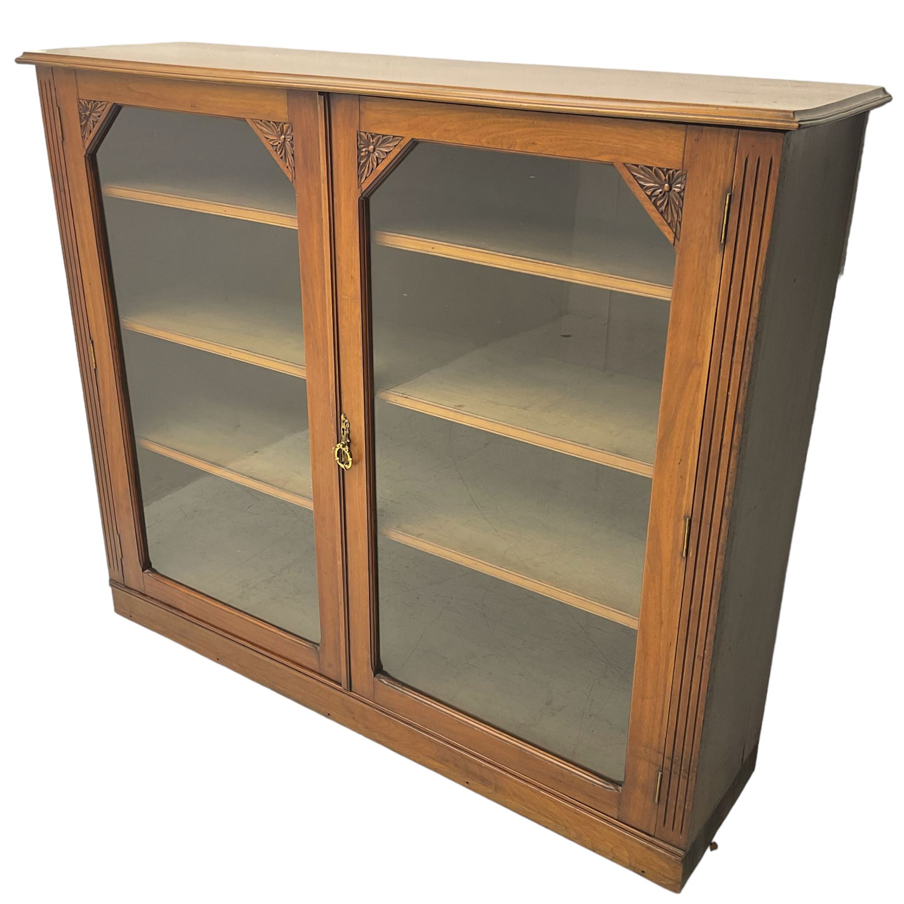 Edwardian walnut bookcase display cabinet, fitted with two glazed doors enclosing six adjustable shelves, flanked by floral carved corners and fluted uprights 