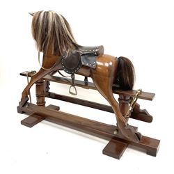 Victorian style stained hardwood rocking horse, complete with studded saddle and bridle, brass stirrups and rockers, raised on two turned columns and floor stretcher