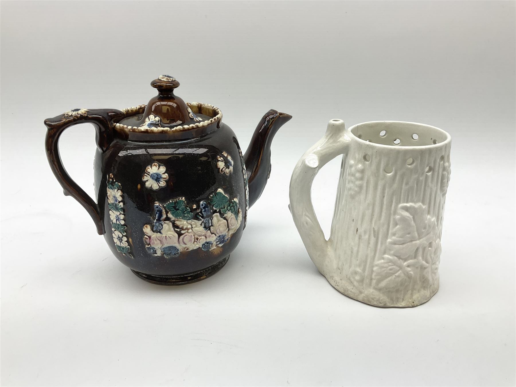 A 19th century Barge Ware teapot, decorated with applied floral sprays and thistles against a mottled brown ground, and plaque detailed Catherine Taylor God Bless Our Home 1890, H18cm, together with a white glazed puzzle mug, H15cm. 