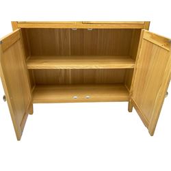 Contemporary light oak display cabinet on cupboard, fitted with two glazed doors enclosing two adjustable glass shelves with light fittings to the top, over panelled cupboard concealing single shelf, on square supports