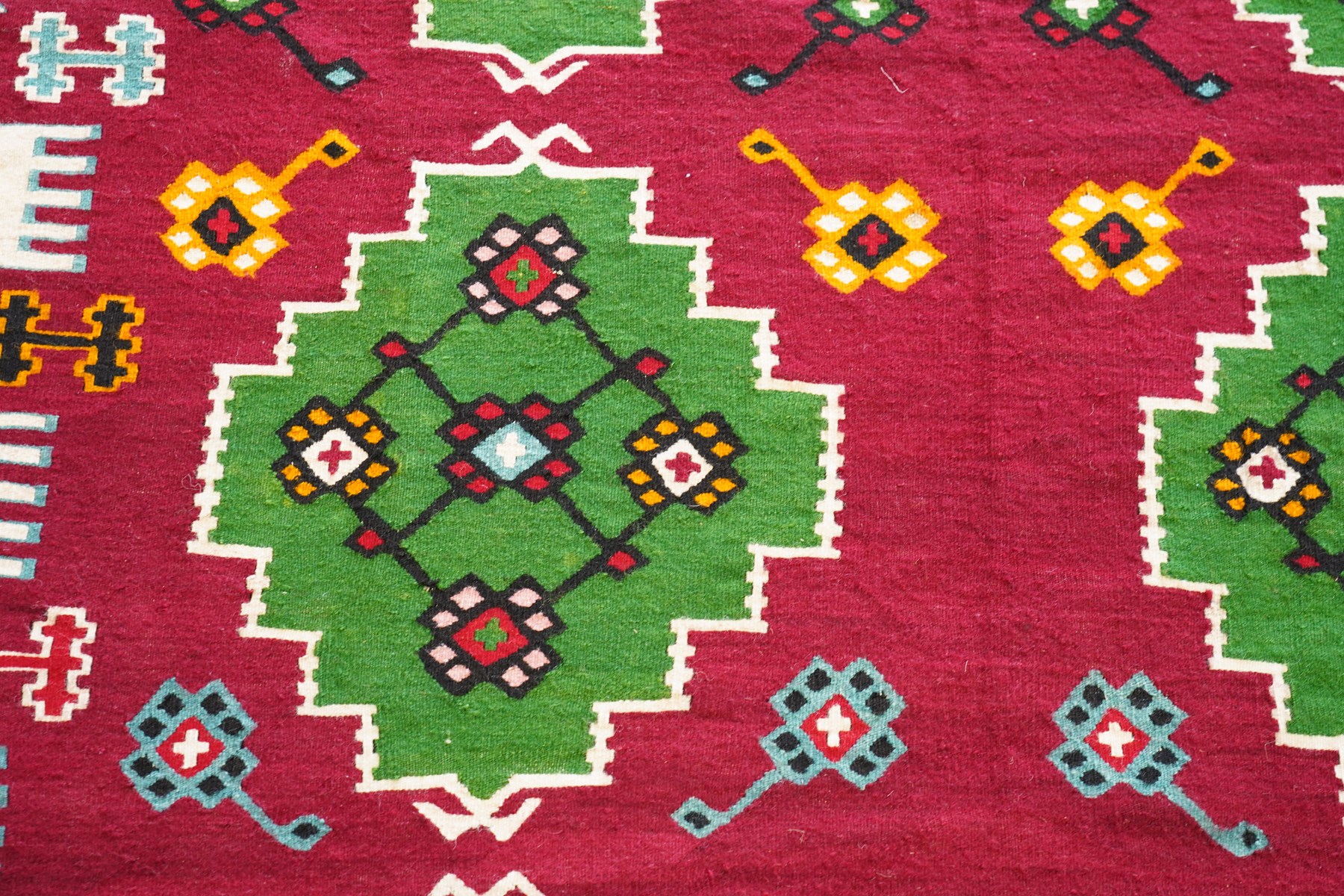 Persian Fars province crimson ground kilim rug, decorated with two rows of geometric emerald green motifs containing stylised plant designs, enclosed by an ivory and dark indigo guard band