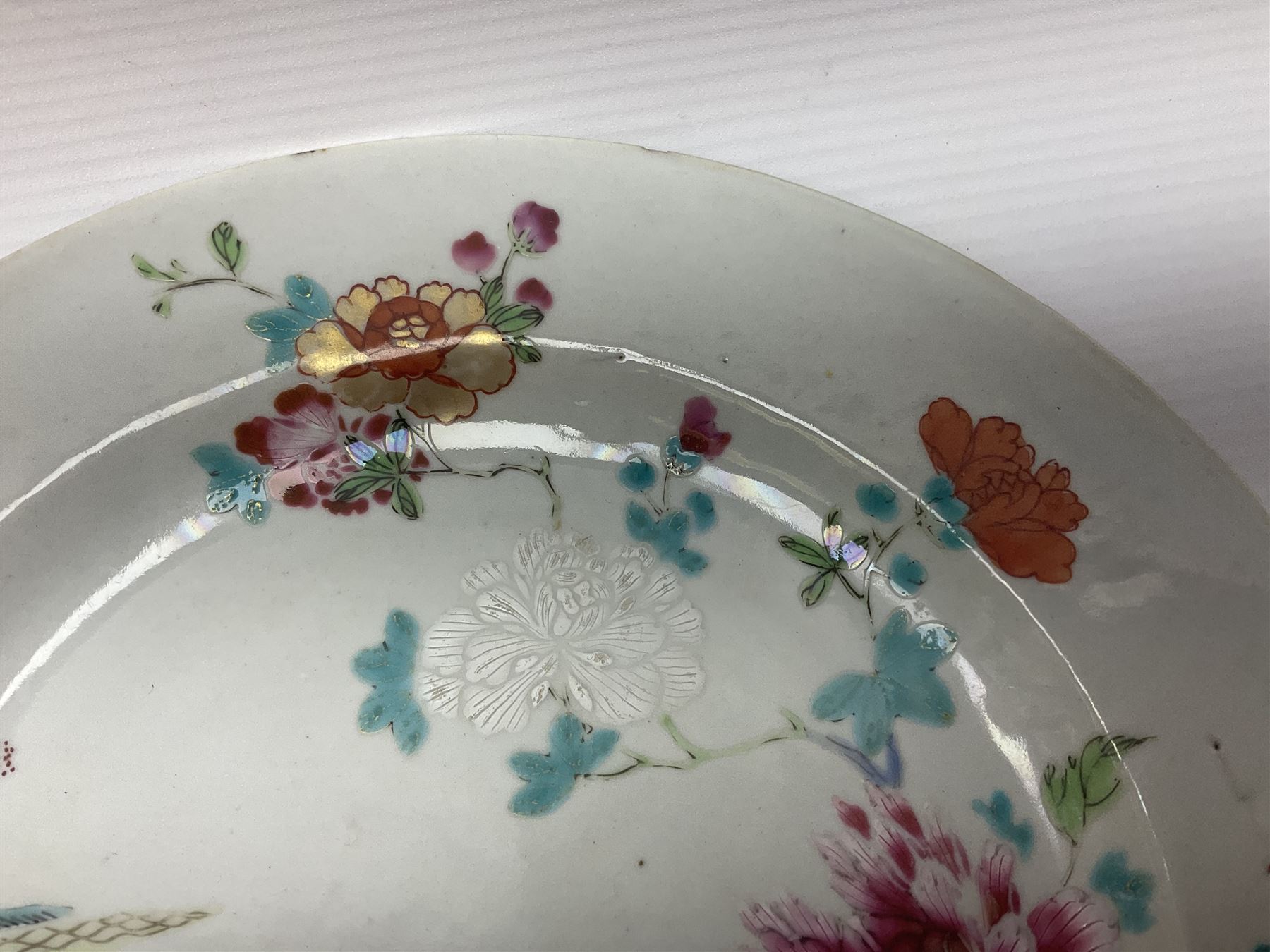 Three 18th century Chinese Famille Rose plates, the first example enamelled with blossoming peonies, rockwork and fence, the other two examples of similar design, decorated with blossoming peonies and sprigs within shaped inner borders, each approximately D23cm