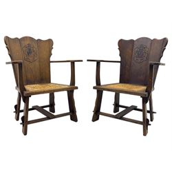 Pair of Arts and Crafts oak armchairs each with shaped backrest centred by polychrome painted crest, rush seat over straight square legs united by shaped central stretcher