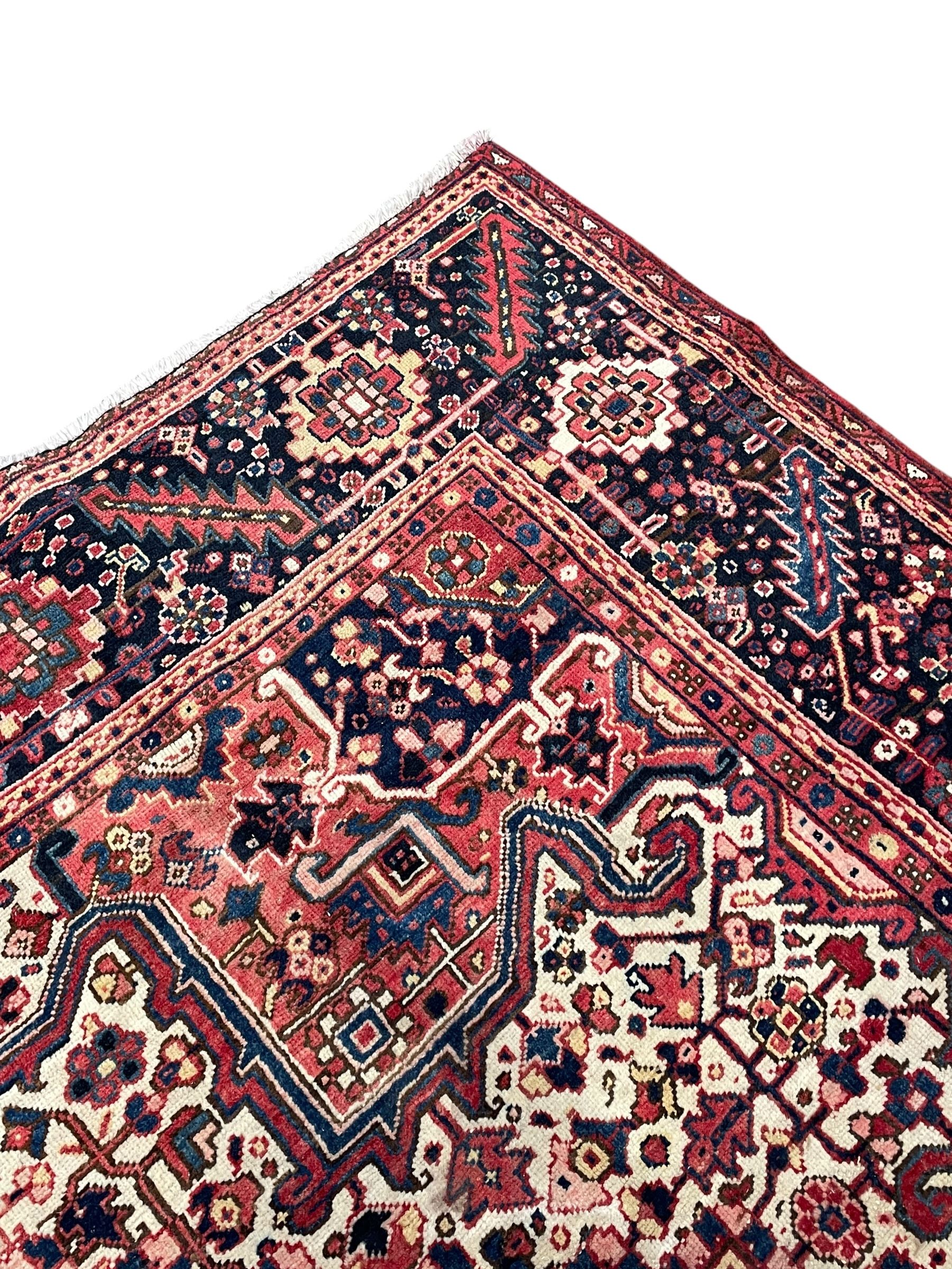Persian Heriz crimson ground carpet, large central medallion comprising projecting palmettes with surrounding stylised plant motifs and trailing branches, the main border decorated with stylised leaf and flower head motifs within geometric pattern guard stripes