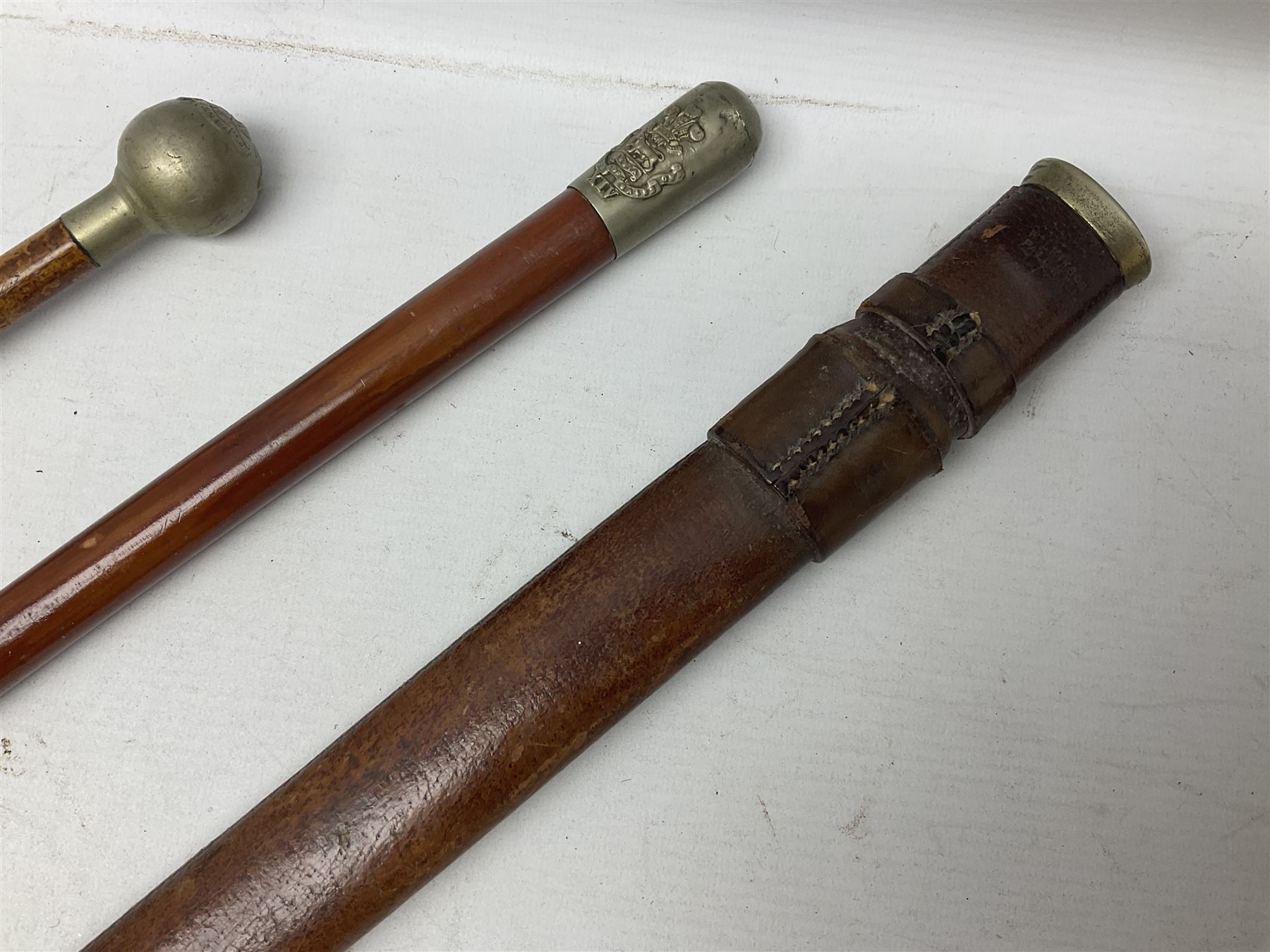 George V 1897 pattern Army Officer's sword by Henry Wilkinson Pall Mall London, the 82.5cm 'London Made' blade etched to both sides with Royal Crests and cyphers etc, pierced half-basket hilt with wire-bound fish skin grip and remains of leather knot strap; in leather covered field service scabbard L101cm overall; and two 14th Prince of Wales Own swagger sticks (3)