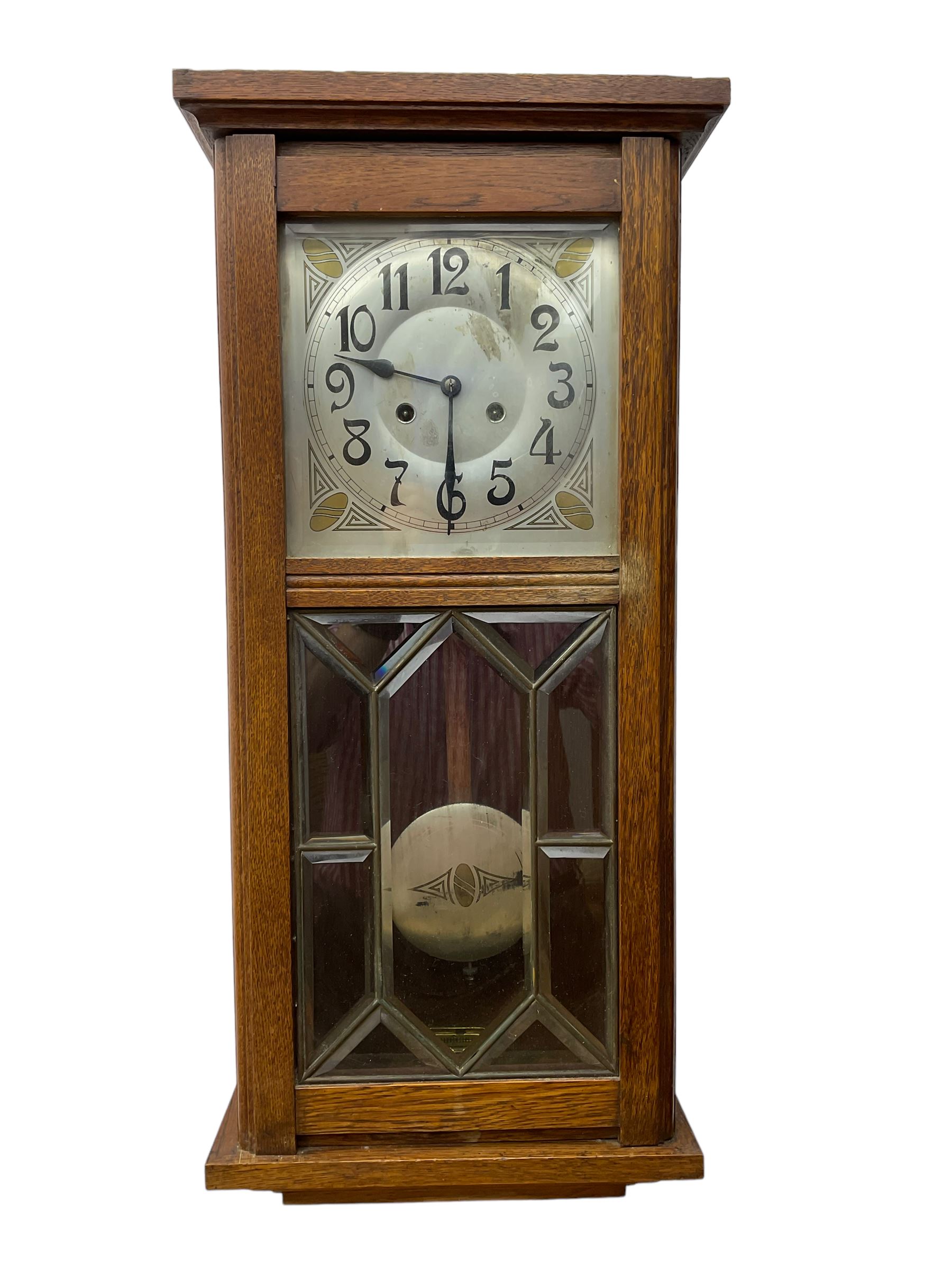 German - Art Deco oak cased 8-day wall clock c 1930, with a moulded flat top and fully glazed door, deeply cut bevelled glass panels and visible pendulum, silvered dial with Art Deco design spandrels, Arabic numerals, minute track and spade hands, twin train movement striking the hours and half hours on four gong rods. With pendulum and key.  