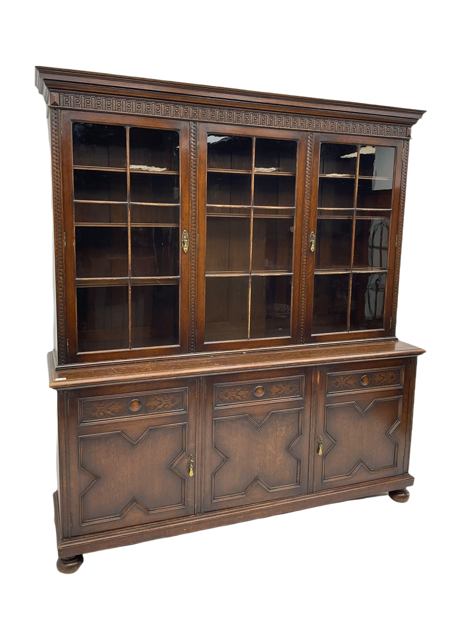 Waring and Gillow - oak bookcase on cupboard, projecting cornice over arcade frieze, guilloche upright decoration, the top section enclosed by three astragal glazed doors, the lower section enclosed by three geometric panelled doors with blind fretwork decoration, on turned feet