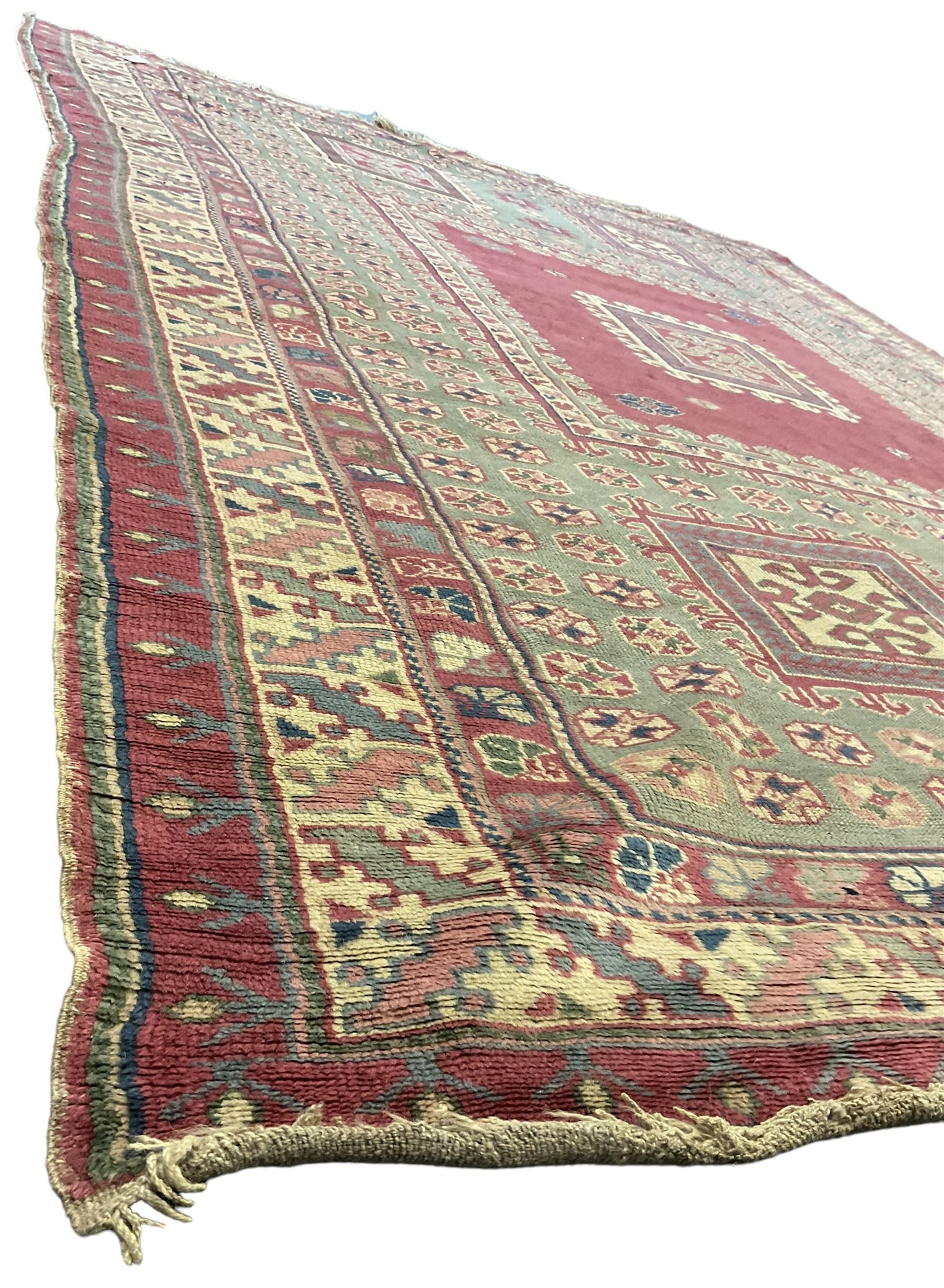 Turkish deep pink and green ground carpet, the square field with hooked borders surrounded by geometric motifs, multi-band border with overall geometric designs 