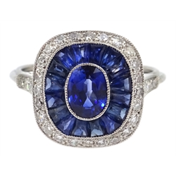  Platinum (tested) ring set with central oval sapphire, halo of calibre cut sapphires and a diamond surround, with diamond shoulders  
