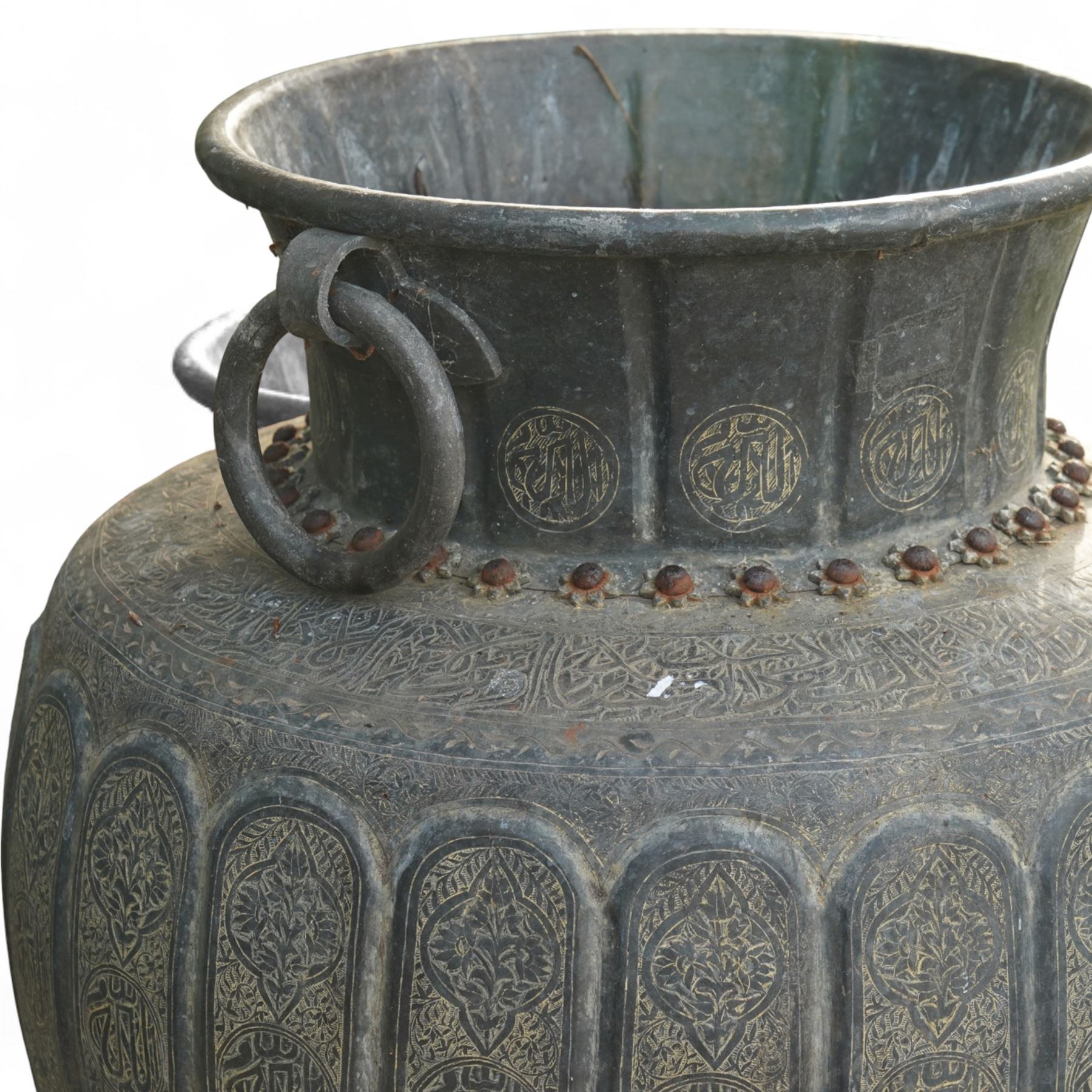 Pair of large Indian cast metal garden urns, each of bulbous form with engraved foliate and script panels, twin ring handles to the neck, raised on fluted pedestal bases