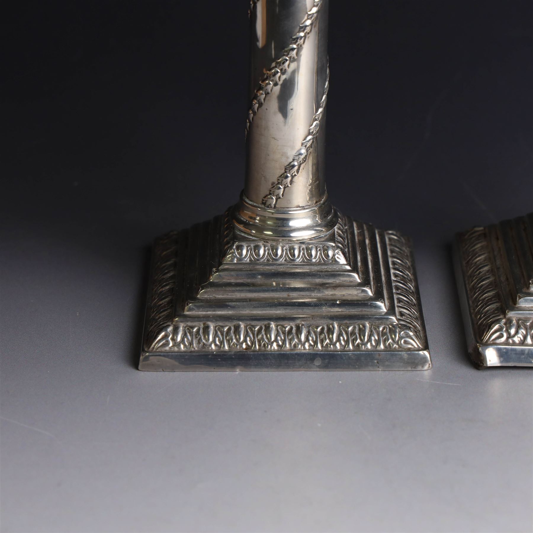 Pair of Edwardian silver mounted column candlesticks, each with embossed floral, foliate and scrolling decoration and upon stepped square weighted bases, hallmarked William Hutton & Sons Ltd, London 1901, H19cm