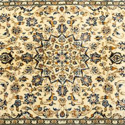 Central Persian Kashan hand-knotted rug, ivory ground, with a small central floral medallion and pendants, the field decorated with fine blue, ochre and beige scrolling vines, flowerheads and palmettes, within an ivory border of repeating floral sprays and meandering vines, flanked by narrow guard stripes, with cotton fringes