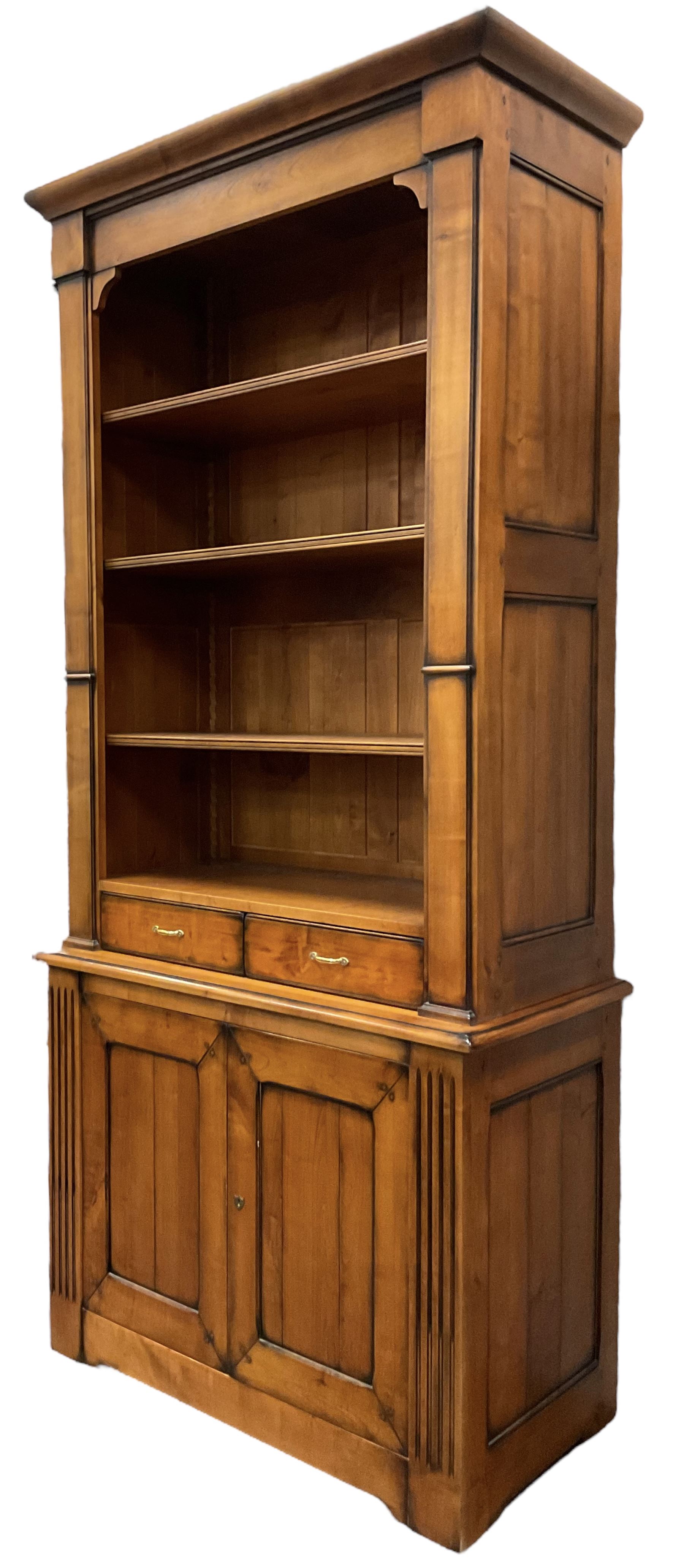 French cherry wood bookcase on cupboard, projecting moulded cornice over three shelves and two small drawers, the cupboard enclosed by two panelled doors flanked by fluted uprights