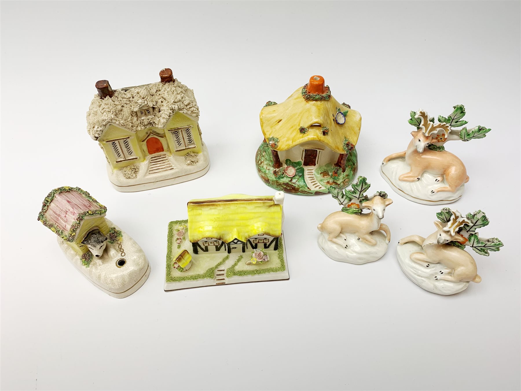 A group of Victorian and later figures, comprising Victorian Staffordshire money box in the form of a house, a Victorian Staffordshire pastille burner in the form of a house, three figures modelled as recumbent deer before trees, Staffordshire style model of a dog emerging from a kennel upon pen holder base, and Coalport pastille burned in the form of a house. (7). 