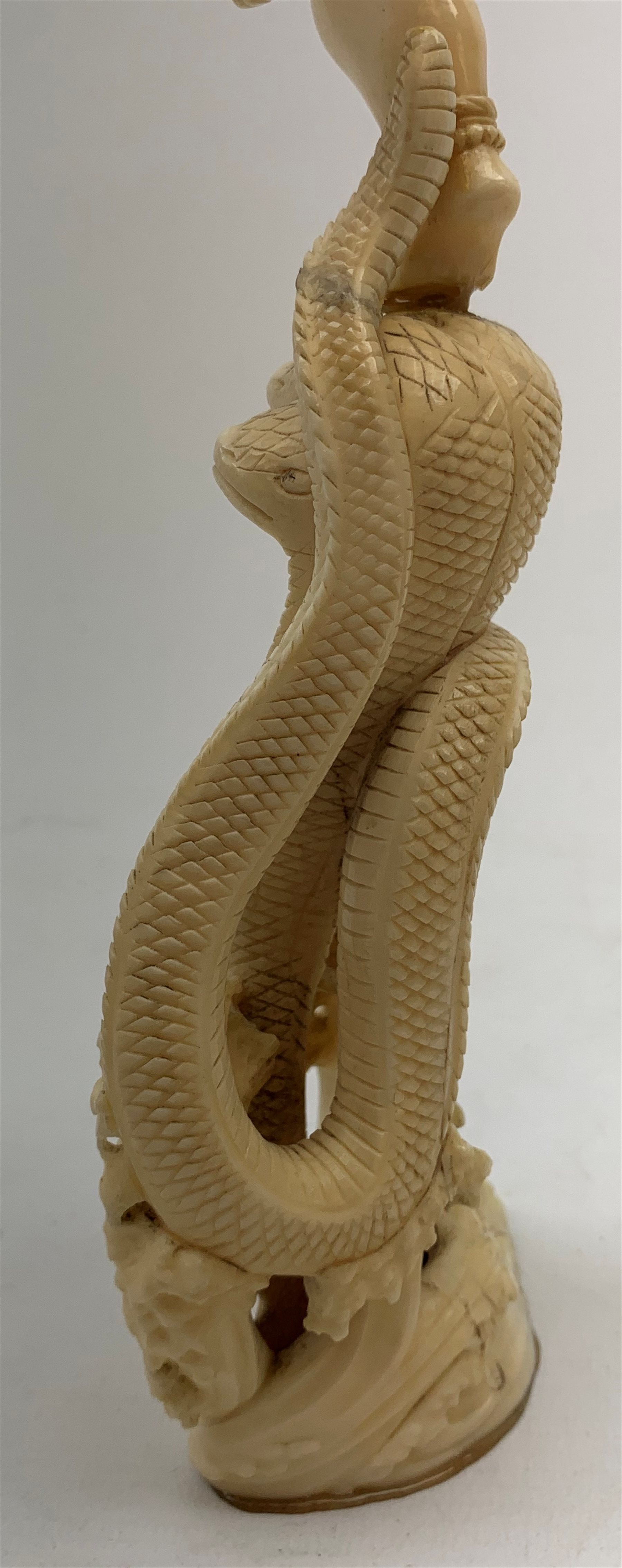 A large Japanese carved ivory okimono, modelled as a figure stood upon one leg with arms outstretched, upon a five headed serpent emerging from waves, H30cm.