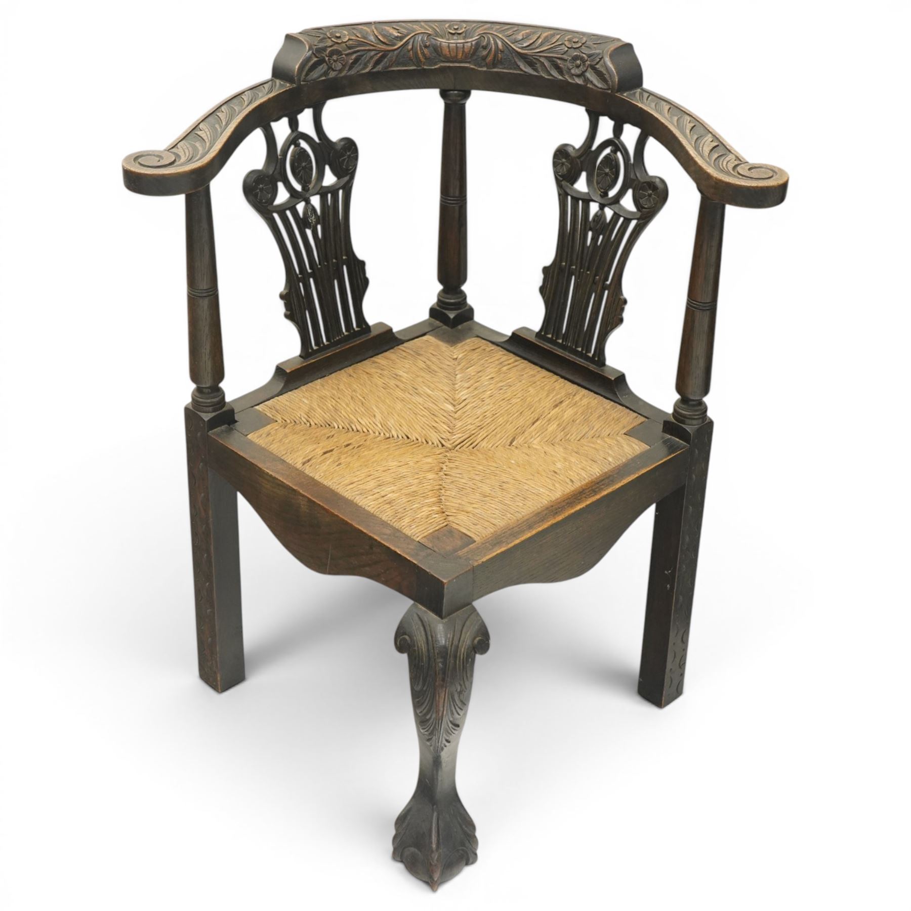 Pair of 19th century carved oak corner chairs, cresting rail carved with central floral bouquet with trailing foliage extending to the scroll arm terminals, pierced back splats with rosette motifs over drop-in rush seats, front cabriole support with acanthus carved knee and ball-and-claw foot