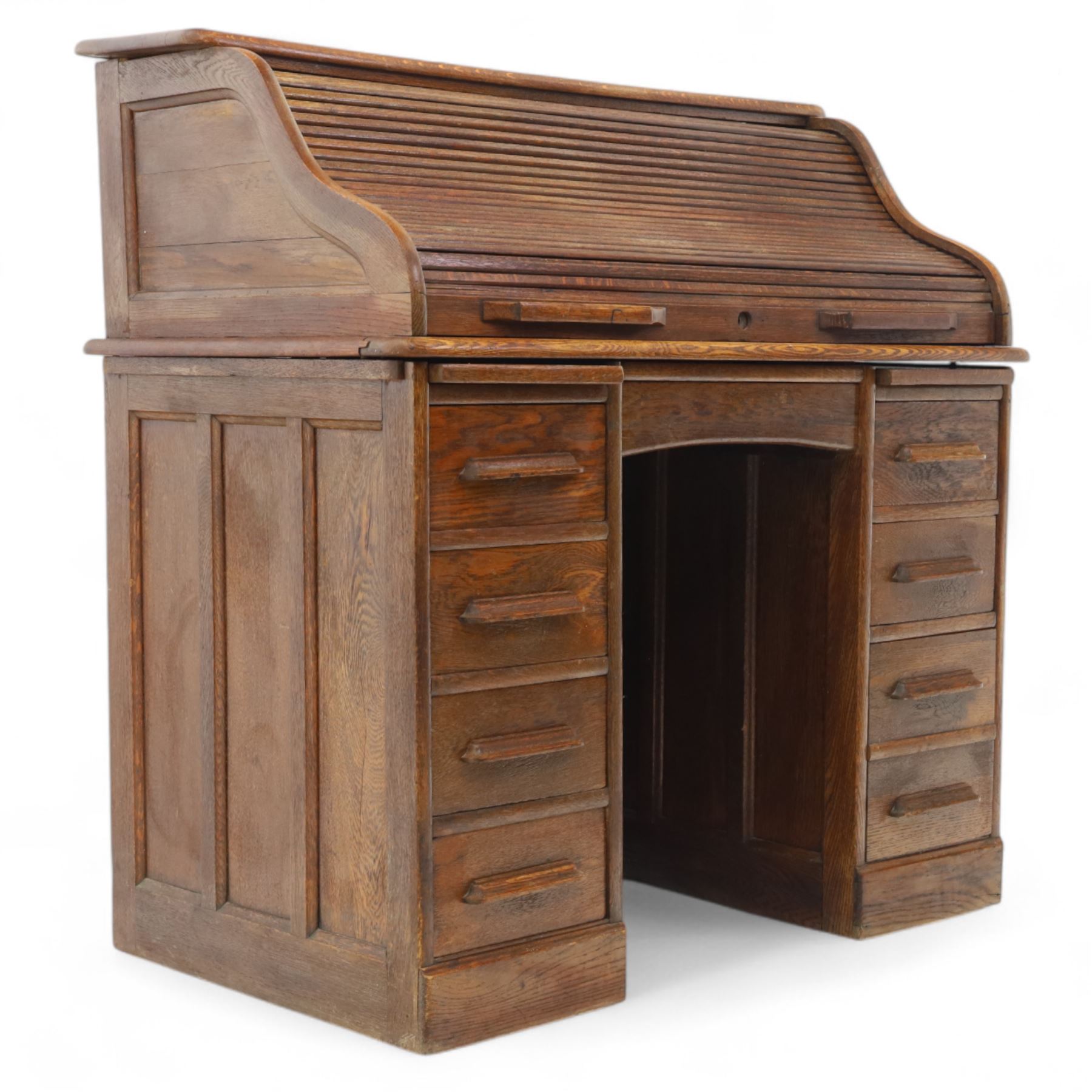 Early 20th-century oak roll-top desk with tambour shutter, enclosing a fitted interior of pigeon holes and small drawers, and pedestal base fitted with nine drawers with moulded handles, raised on plinth base 