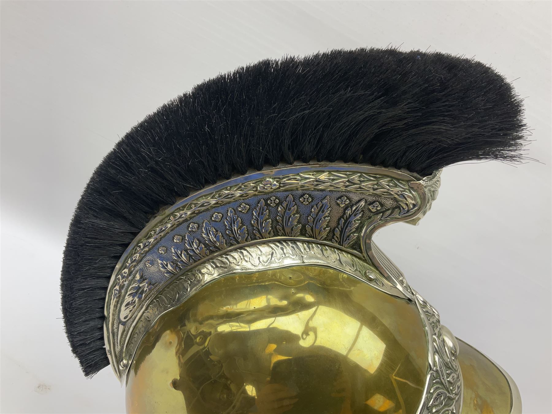 Early 20th century French mounted gendarme's helmet, brass with nickel-silver mountings, broad band embossed with fused grenade, high comb with the face of the gorgon Medusa at the peak and with a black horse hair crest, plume socket at the left, leather-backed nickel-silver chin scales with lion mask mounts.