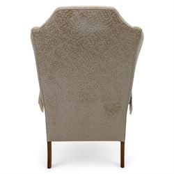 Late 20th century wingback armchair and matching footstool, upholstered in beige embossed fabric with brass stud edging, on cabriole legs and splayed rear legs, together with a matching footstool on turned supports terminating in brass castors (Stool H 42cm, W 75cm, D 47cm)