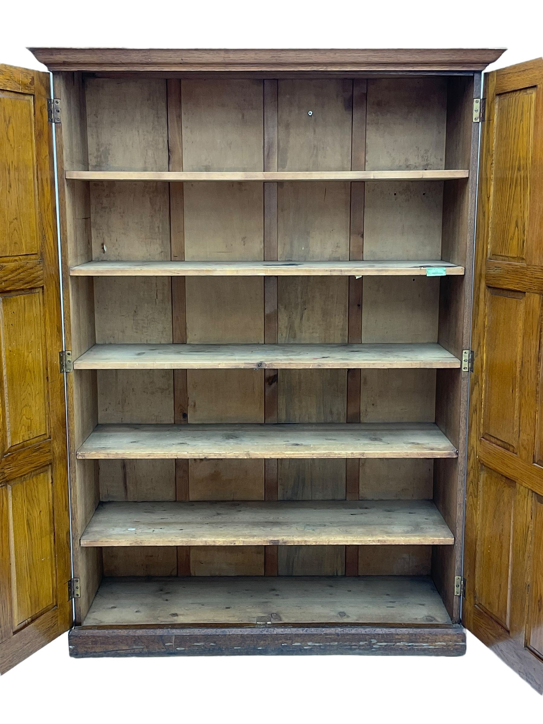 The North of England School Furnishing Company Limited Darlington - early 20th century oak school cupboard, projecting moulded cornice over two panelled doors, fitted with shelves, on chamfered plinth base 