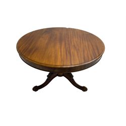 19th century mahogany breakfast table, the banded circular top on turned column pedestal, three scroll and foliate carved cabriole supports terminating in brass castors