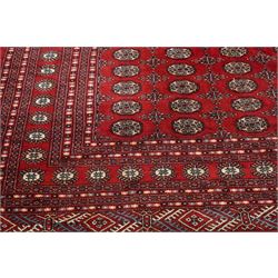 Large crimson ground Afghan Bokhara carpet, the field decorated with repeating Gul and geometric motifs, the multiple guard stripes with further geometric decoration