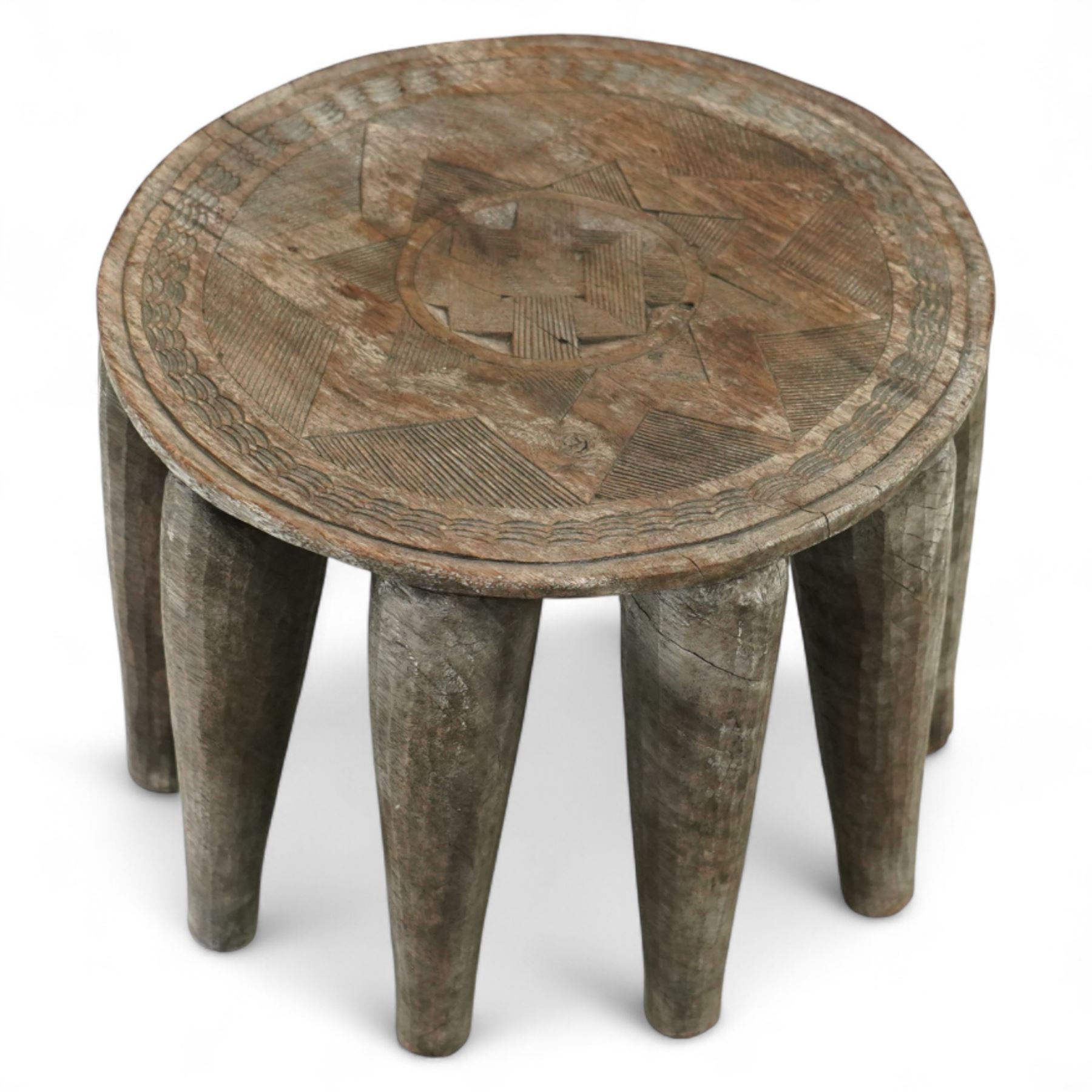 African Nupe carved tribal stool, the rounded top with repeating incised decoration and rope-edge border, supported by ten tapered legs D37cm
