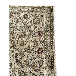 Persian Kashan ivory ground carpet, central medallion decorated with sixteen arranged palmette motifs, within a field decorated with swirling leafy branches and stylised plant motifs, the main border decorated with matching swirling pattern, within floral pattern guard stripes 