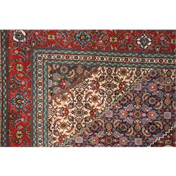 North West Persian Tabriz hand-knotted rug, ivory field with a central lozenge shaped medallion in indigo and madder red, issuing an ornamented arrangement of Herati style motifs, rosettes and angular floral elements, conforming spandrels on an ivory ground, main border in madder red with stylized vinery and palmettes, flanked by multiple guard border, with cotton fringe ends 