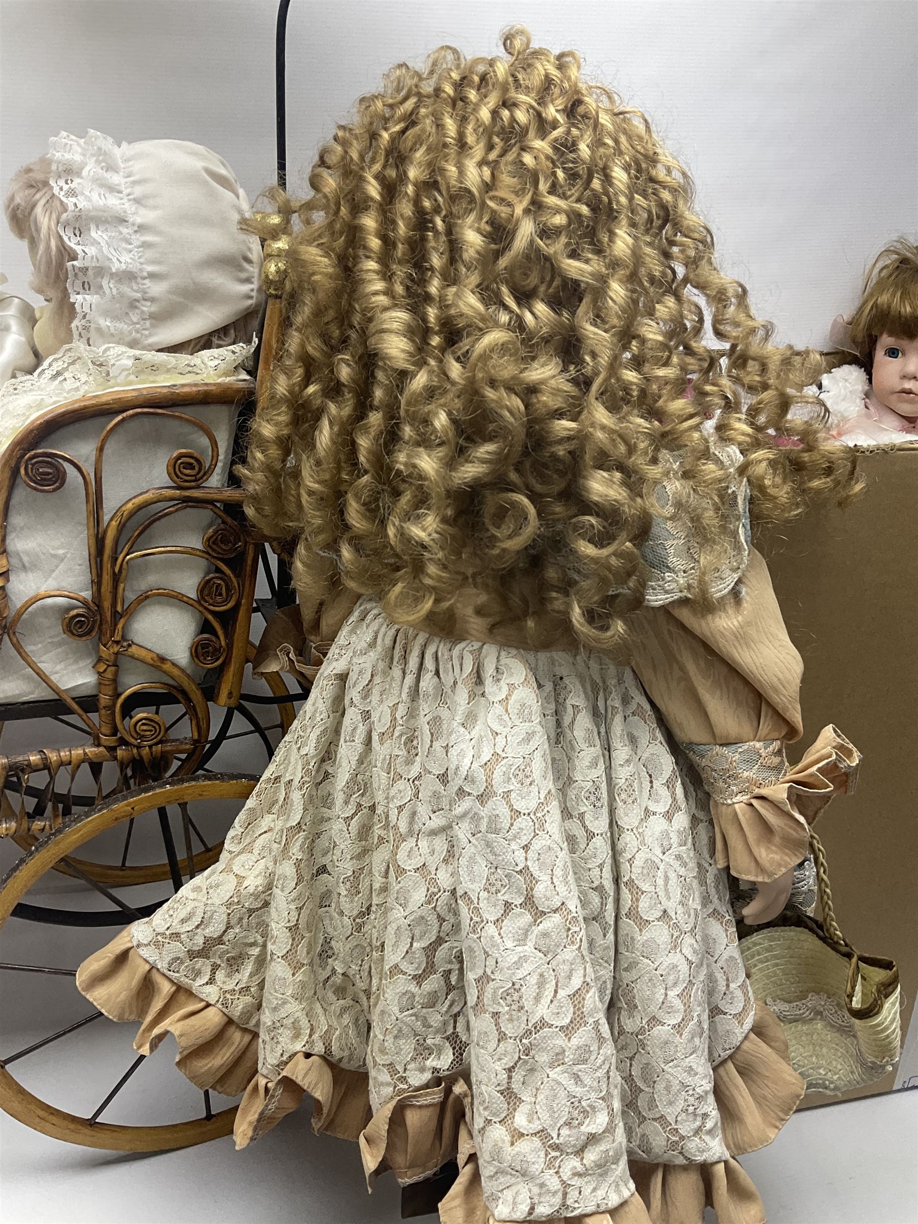 Two decorative wicker dolls prams, one with lace parasol,  and eleven dolls, including Leonardo Collection porcelain dolls, tallest pram including parasol H105cm