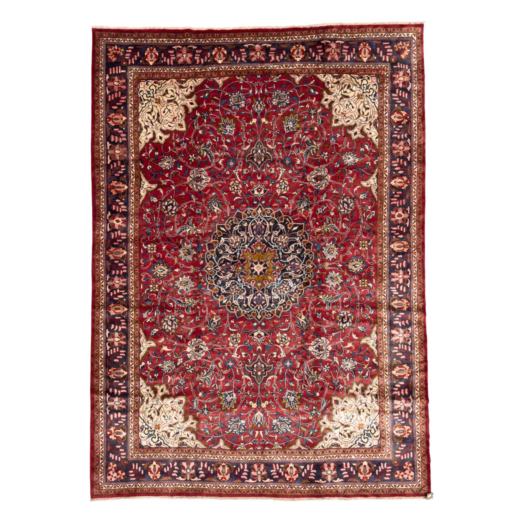 Northwestern Persian Lillihan hand-knotted carpet, madder red field with scrolling vines, rosettes, and palmettes around a central circular medallion in navy, ivory and ochre, and ivory ground spandrels within a navy border of stylized flowerheads and vines between multiple guard stripes 