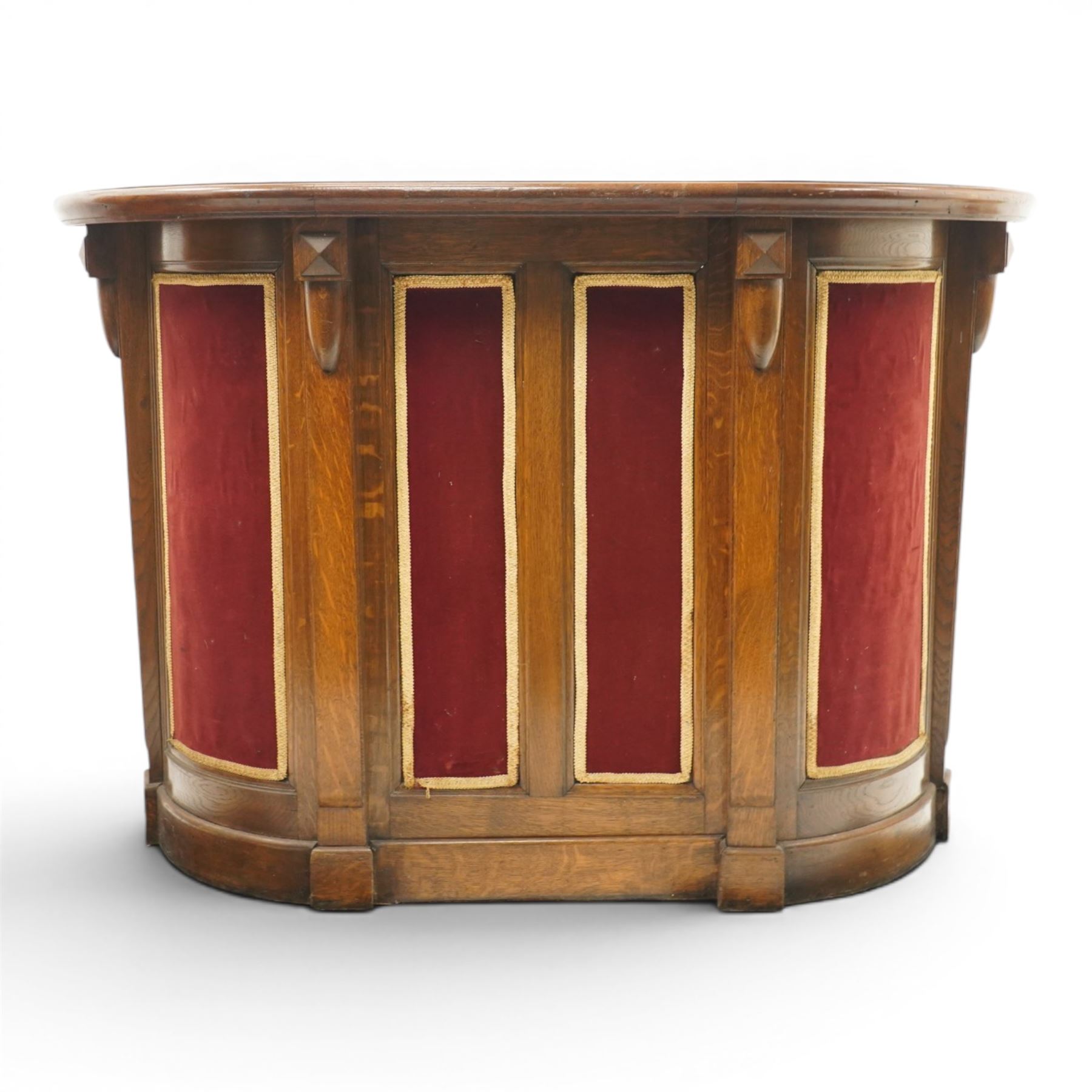 Arts & Crafts oak D-shaped bar, moulded edged counter above a front with velvet applied panels, the back with shelving, raised on a plinth base