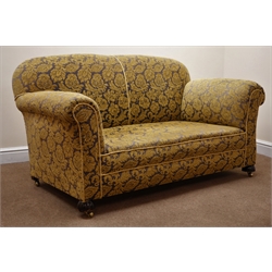  Victorian two seat drop arm sofa, upholstered in floral patterned gold and gun metal coloured fabric, turned supports on brass castors, W155cm   