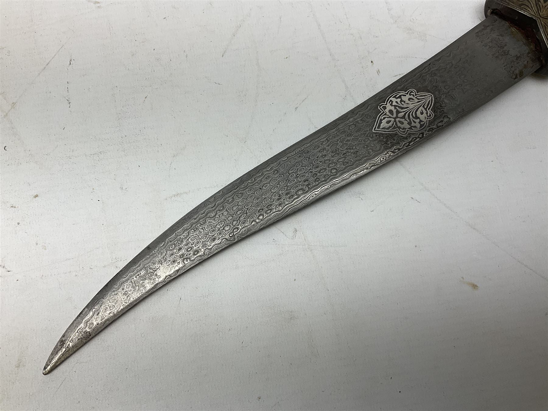 Indian Khanjar dagger with 28cm curving damascus steel blade inlaid with silver floral emblem, white metal and niello style grip in the form of a bird's head with pronounced beak and matching scabbard L44cm overall