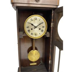 1930s wall clock in an oak case with a crested pediment and glazed door with visible pendulum, silvered dial with Roman numerals and steel spade hands, eight day spring driven movement striking the hours and half hours on a gong. With pendulum and key.
