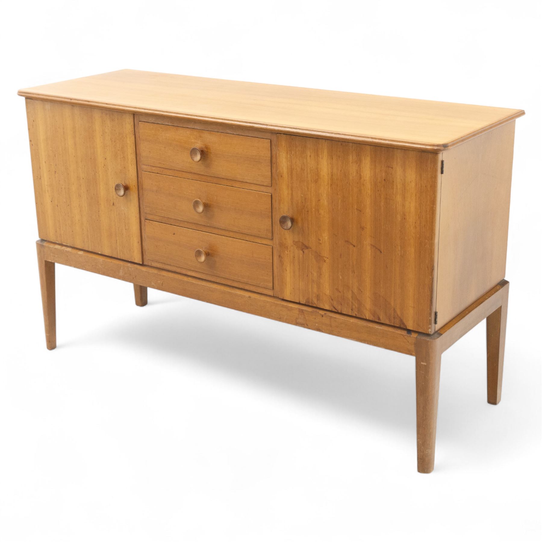 Gordon Russell - mid century modern teak sideboard, the rectangular top with rounded edges over twin cupboards and three central drawers, fitted with circular wooden pulls, on tapered supports, reflecting the firm’s commitment to simplicity and quality materials during the post-war design period