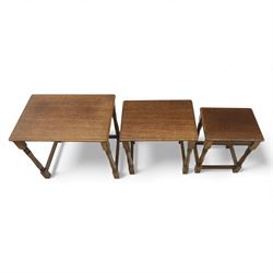 Nest of three dark oak tables, rectangular top with turned supports, tables suspended on rails