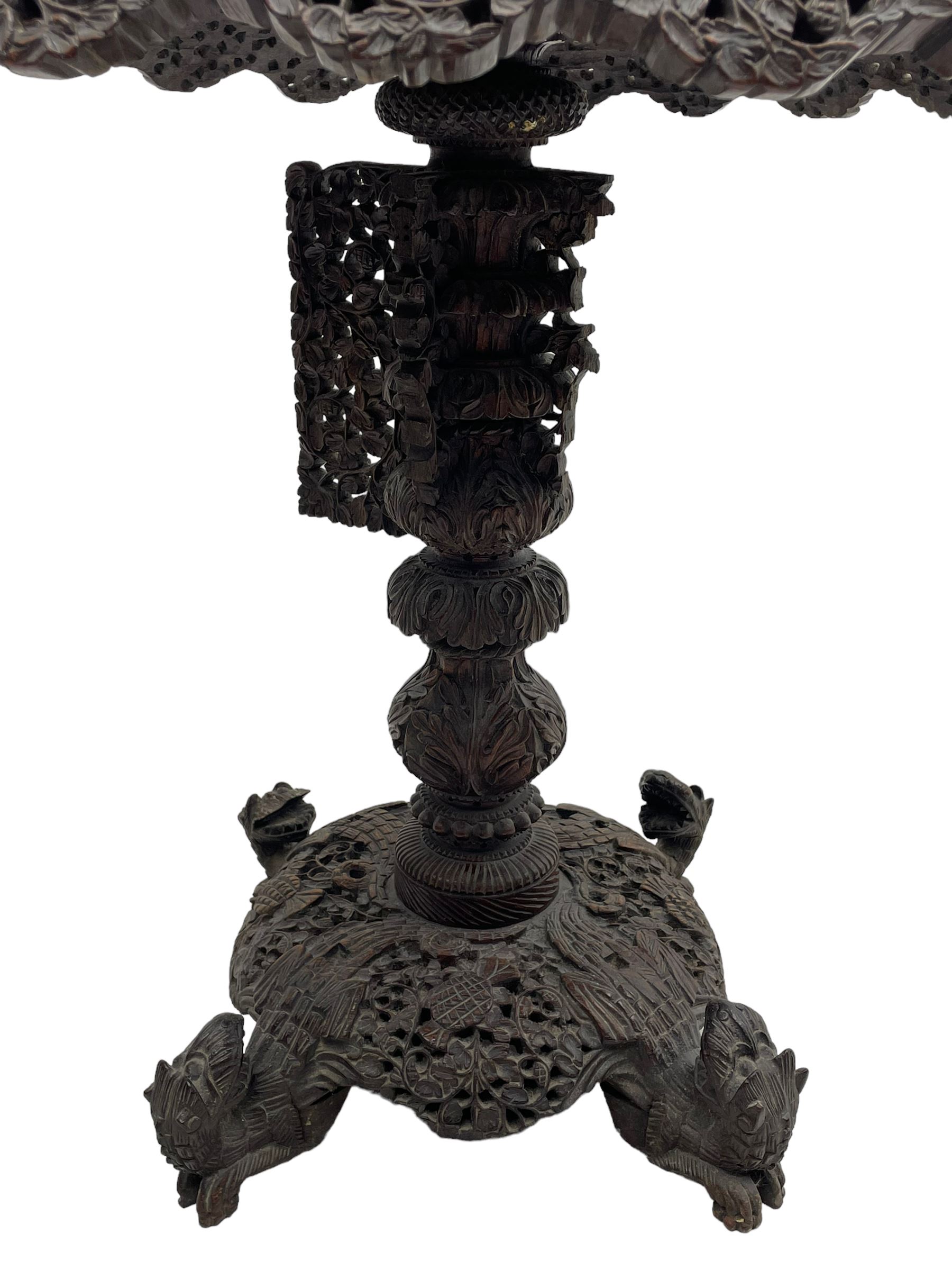 Late 19th century Anglo-Indian carved hardwood occasional table, circular tilt-top carved profusely with mythical animals and foliage decoration, pierced and carved with interlaced leafy branches, leaf carved pedestal supports on a raised platform with further carved and pierced foliage decoration, four carved feet in the form of mythical beasts with gaping jaws 